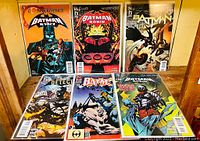 Six Batman-themed DC Comics comic books displayed upright, showing front covers with various Batman artwork and titles.
