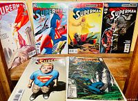 Six Superman comics from DC Comics arranged side by side showing front covers with various characters including Superman and Batman.