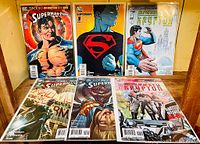 Overview image showing six Superman-related DC Comics comic books arranged on a wooden shelf or surface.