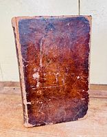 Full cover of worn brown leather book with markings and wear spots.