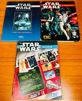 Three Star Wars roleplaying game hardcover books on wooden surface showing titles and cover art.