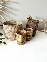 Four wicker baskets of different sizes and styles arranged on white surface against neutral wall with rattan sunburst decoration.