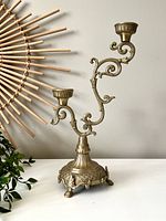 Full view of the brass multi-level candlestick holder with ornate curved arms, pedestal base, and two candle cups.