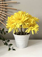 Side view of yellow faux flower arrangement in ribbed white pot on a white surface, with other elements in the background for scale.