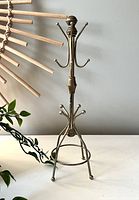 Full view of gold coloured metal jewellery holder showing base, middle and upper hooks, placed on white surface with grey wall background.