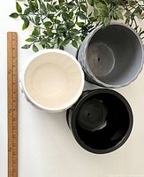 Top-down view showing interior of white, black, and grey ceramic planters and drainage holes in black and grey pots.