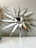 Full frontal view of starburst wall clock showing mirrored rays and black clock hands on silver center.