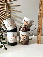 Four coffee mugs stacked and leaning against a ruler showing height about 3.5-4 inches.