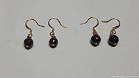 Photo showing two pairs of handmade artisan brass drop earrings with red garnet beads, displayed side by side on a white surface.