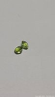 Two pear-shaped apple green peridot gemstones placed on a white background showing clarity and cut.