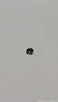 Round cut green sapphire on plain background showing cut and color.