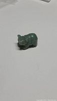 Top and side view of small hand carved green aventurine bear figurine on a white background, showing detail and shape.