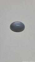 Oval smoky silver moonstone cabochon showing cat's eye effect and flash, viewed from a side angle on white background.