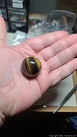 Photo showing the tigerseye sphere held in a person's hand, highlighting its size relative to hand and its polished golden-brown chatoyant surface.