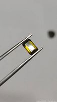 Close-up of emerald cut green tourmaline held by tweezers showing clarity and color