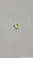 Clear photo showing the oval cut apple green peridot gemstone on a gray background, emphasizing its color and size.