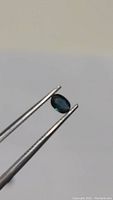 Close-up of small natural blue sapphire held by tweezers with visible blue hue and clarity.