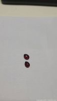 Two pear-shaped cherry red garnet stones on white background showing size and shape.