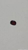 Photo displaying natural cherry red garnet gemstone with deep red color and oval cut shape on a white background.