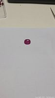 Oval cut natural ruby gemstone on white background showing deep pink reddish color, oval shape, and polished faceted surface.