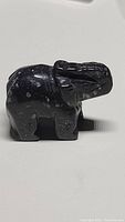 Photo of a small, dark hand carved gemstone elephant figurine with white speckles, showing side profile and detailed carving.