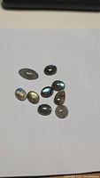 Nine natural labradorite gemstones arranged on a white background, displaying their mixed cabochon cuts and vivid blue and golden flash.