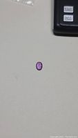 Photo of a single oval cut purple amethyst gemstone on a neutral background showing its clarity and color.