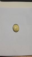 Top view photo of the oval cabochon lemon quartz gemstone on white background showing smooth polished bright yellow surface and translucence.