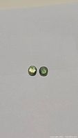 Two oval cut natural green sapphires displayed on plain white background, showing slight color differences.