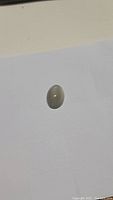 Oval cabochon shaped natural moonstone with smooth polished surface, displaying smokey silver coloration and slight cat's eye flash.
