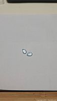 Pair of pear cut sky blue topaz gemstones on white paper background showing size and color.