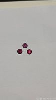 Three round faceted natural Rhodolite garnet gemstones in deep reddish-purple color, approximately 5mm each, shown on white background