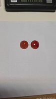 Front view of two round orange Carnelian cabochon gemstones on white background with scale.