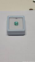 Top view of natural 1.27 carat Colombian emerald loose in white display box, showing emerald cut, vivid green color and luster.