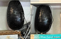 Pair of modern black metal oval-shaped lamps with perforated patterns laid side by side showing cords and plugs.