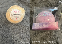 Two bath bombs side by side, one orange labeled Aphrodisiac Bath Bomb and one sealed pink Tropical Punch bath bomb.