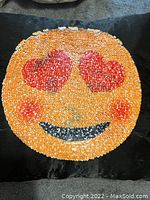 Sequin pillow with heart eyes emoji design on black background.
