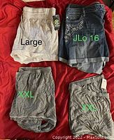 Four pairs of women's shorts laid out on red fabric background, showing two XXL gray Champion PJ shorts, one large gray Champion short, and one size 16 denim JLo shorts with rhinestones.