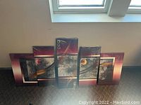 Full view of the five-panel abstract canvas art leaning against wall beneath skylight showing burgundy and gray artistic design with gold accents.