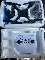 Black drone with camera and white remote controller in foam packaging.