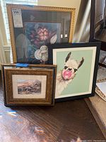 Three framed art prints grouped together, showing floral, countryside, and llama artwork