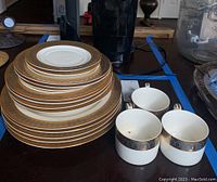 Stack of 16 plates of various sizes with gold and blue decorative borders, displayed next to four matching cups.