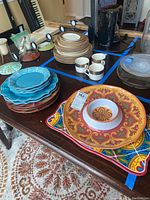 Photo shows various dishes and platters arranged on a table including blue Pioneer Woman dishes, ceramic Pier One serving platters with colorful designs, and melamine platters.