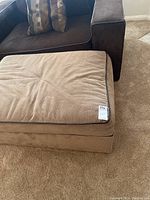 Side and top angled view of a large rectangular ottoman in light brown corduroy fabric with faux leather piping along edges.