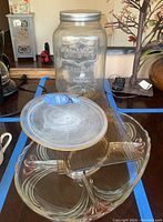 Photo of large clear glass beverage jar with metal lid and parts of the two trays underneath