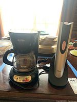 Full view of Mr. Coffee 4-cup coffee maker and Oster electric wine opener side by side on a table with plates in the background.