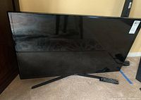 Samsung 40 inch TV on stand with remote visible at base on carpet floor.