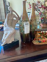 Photo shows two ceramic vases and a ceramic female figurine on a flat surface with flowers in the background.