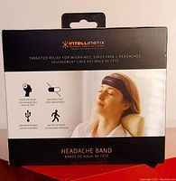 Front of box showing brand name, image of person wearing band, and product features such as drug-free relief, USB rechargeable, and targeted relief for migraines, sinus pain, and headaches.
