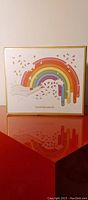 Front view of the closed puzzle box showing the rainbow hand shaped foil design with vibrant colors and Jonathan Adler branding.